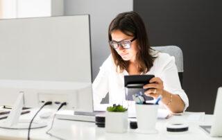 Female accountant sitting at her desk in front of a computer and laptop and holding a calculator in her hand (job opportunities at iGuana)
